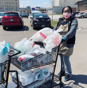 woman wearing mask in a parking lot with a shopping cart of groceries